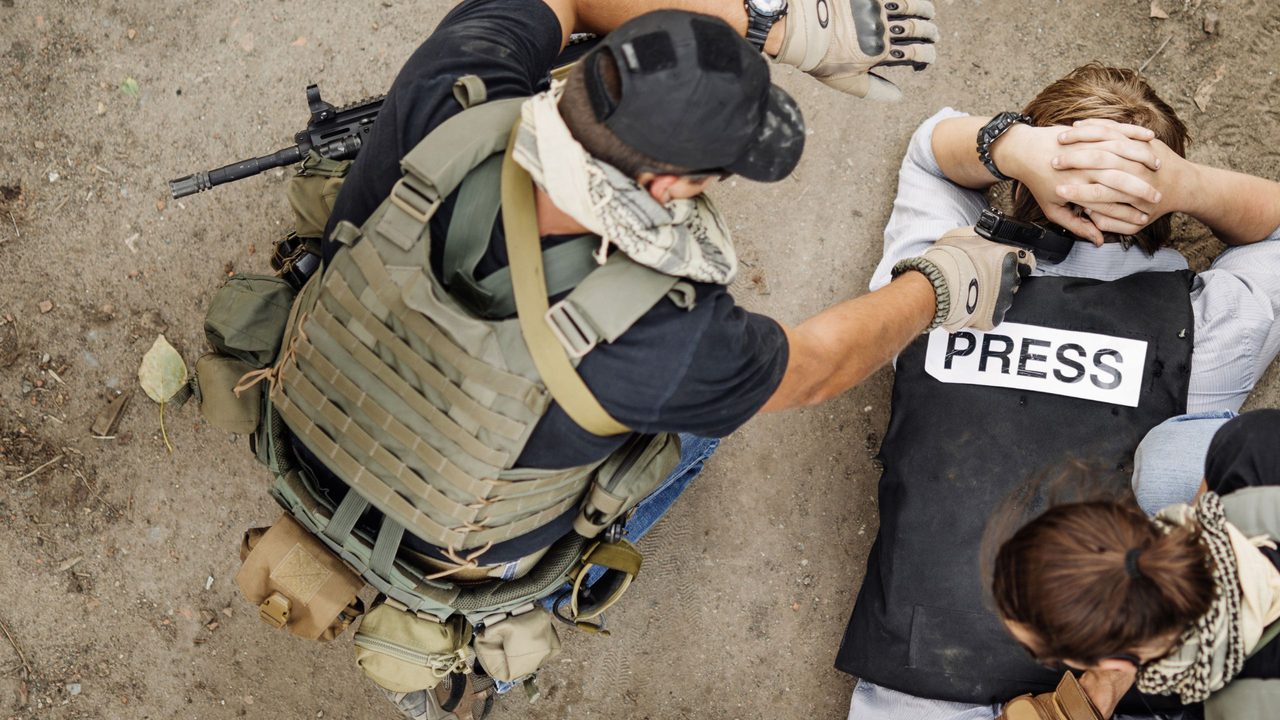 Journalist in a conflict zone lying on the ground wearing a press vest.