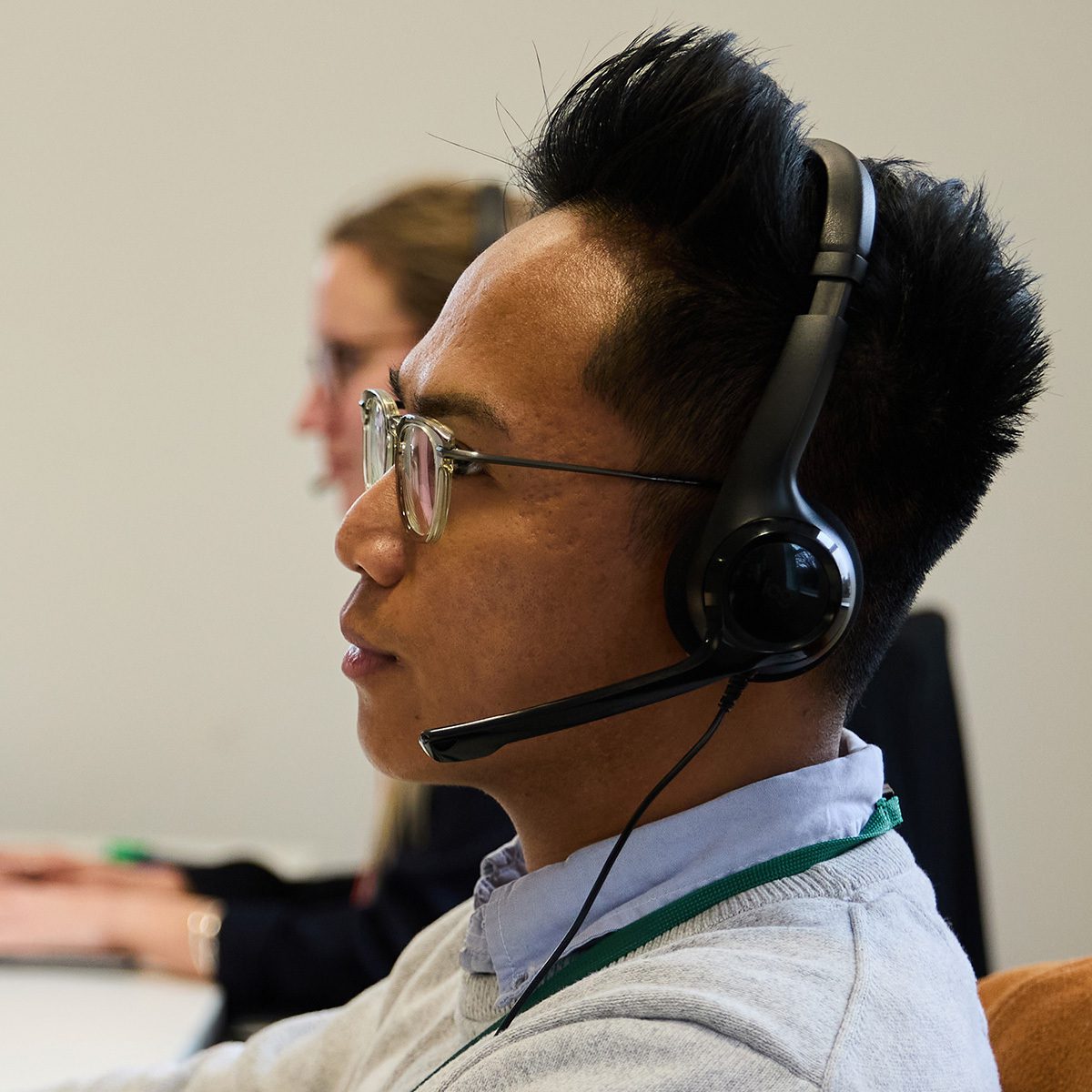 Male call centre agent with headset handling customer enquiries in office environment.