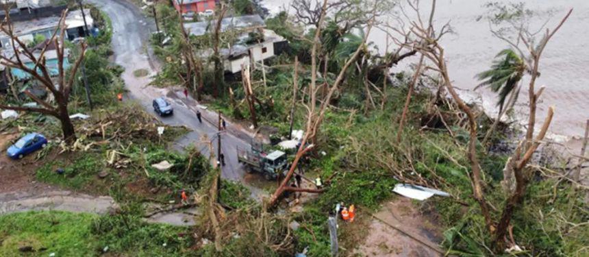 Image showcasing the aftermath of an earthquake on Vanuatu Island. Trees have fallen in the road and telephone poles have fallen down, residents are helping with the clear up.