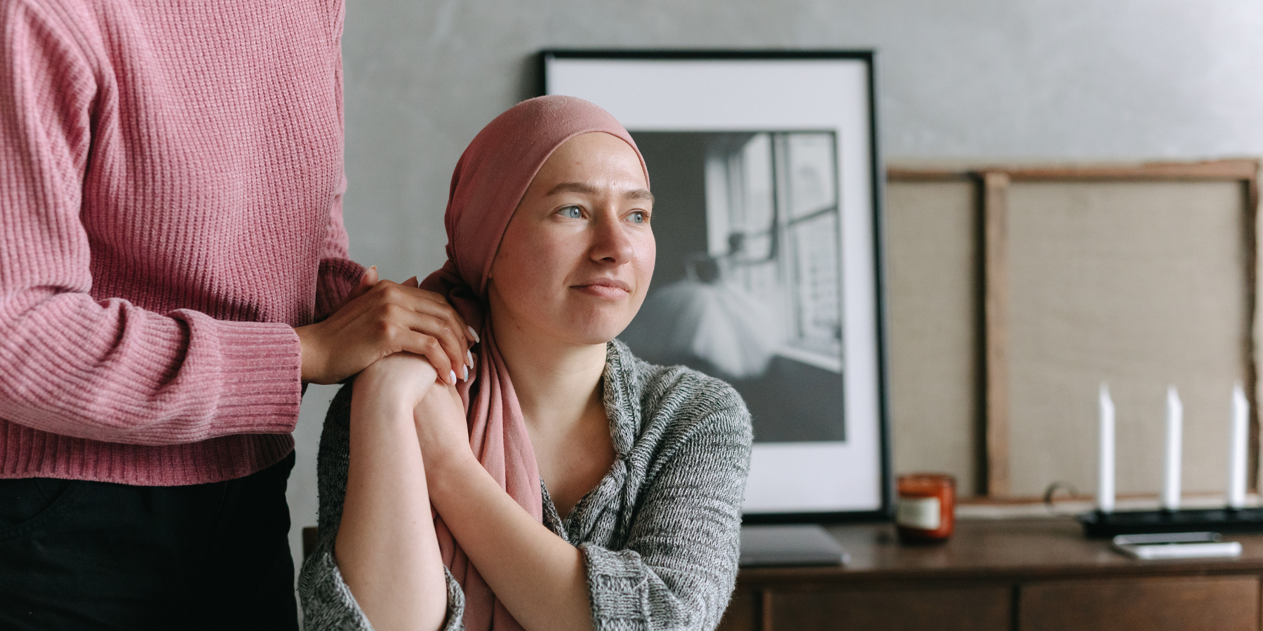 A woman going through cancer treatment being supported by a person resting her hands on her shoulder