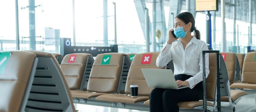 An image of a business woman in an airport wearing a mask and social distancing representing the impact of covid-19 on business travel.