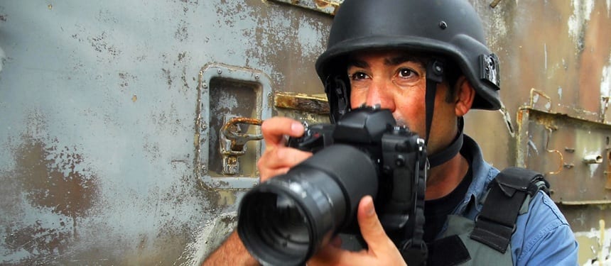 Journalist photographer in protective gear taking a photo in a conflict zone